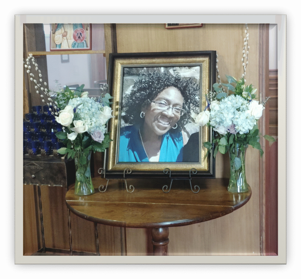 A picture of Corliss Catherine Lawrence in a wooden 16 x 20 frame. Blue and white flower arrangement around her picture